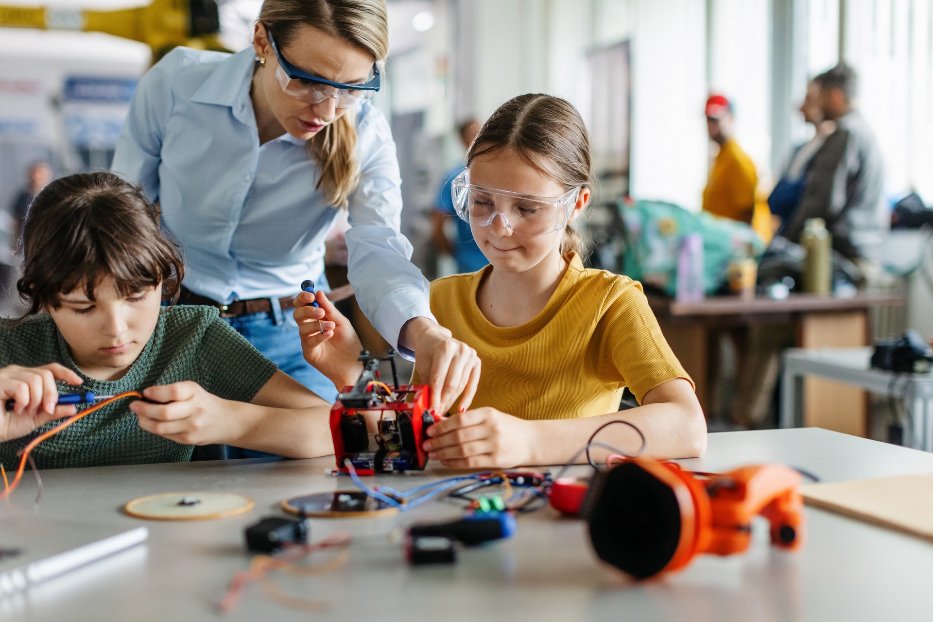 Female teacher helping to girls working on small robot, building robotic car in after-school robotics club. Children learning robotics in Elementary school. Girls in science.